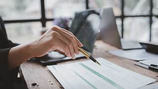 hand with pen marking up paperwork at desk