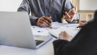 person in business attire at desk with computer open and papers in front of them