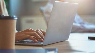 person typing at their desk on laptop with coffee cup